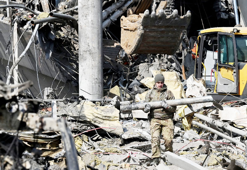 ２４日、ロシア軍による砲撃で破壊されたキエフの建物付近でロケット弾の残骸を手に歩くウクライナ兵（ＡＦＰ時事）