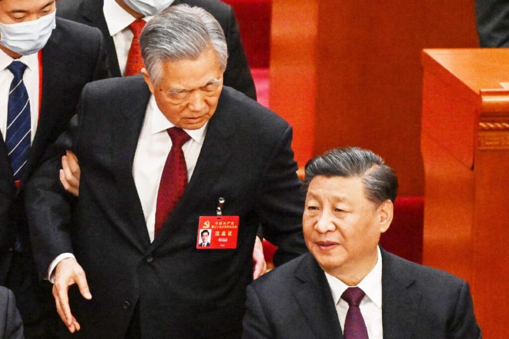 22日、北京の人民大会堂で、中国共産党大会の閉幕式から腕をつかまれて退席する胡錦濤前総書記(中央)(AFP時事)