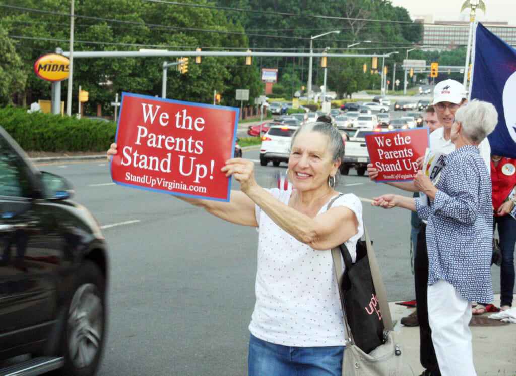 車道を走る車に「われわれ親は立ち上がる!」と書かれたプラカードを掲げるロースさん(山崎洋介撮影)